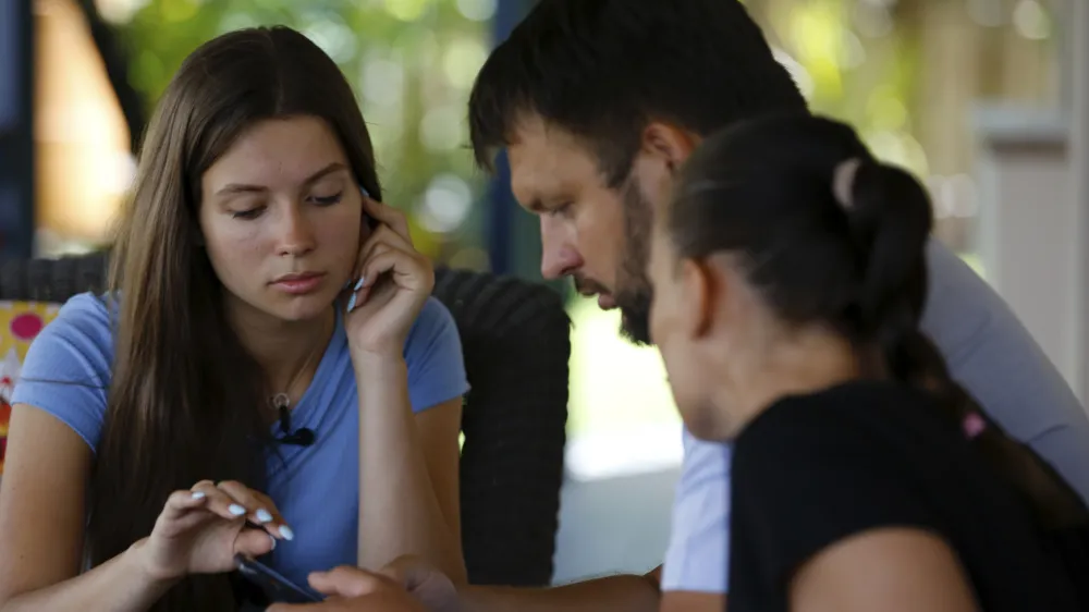 Vasyl Prishchak, center, of Kyiv, Ukraine, looks at photos on his phone with his wife, Marina, right, and daughter Mariia, 16, left, at their temporary home in Kailua, Hawaii, Wednesday, March 23, 2022. The Prishchak family travelled to Hawaii for a long-awaited vacation on Feb. 16 and planned to return to Ukraine on March 7. But a week into their vacation, Russia invaded their country, leaving the family in shocked disbelief with no access to family, friends, money or their home. (AP Photo/Caleb Jones)