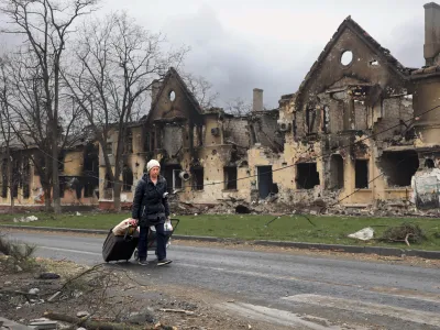 A woman pulls her bags past houses damaged during a fighting in Mariupol, on the territory which is now under the Government of the Donetsk People's Republic control, eastern in Mariupol, Ukraine, Friday, April 8, 2022. (AP Photo/Alexei Alexandrov)