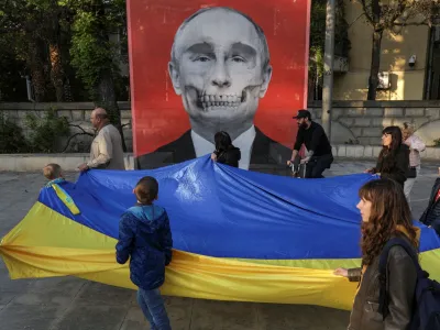Protesters carrying a large Ukrainian flag and heading to a protest against Russia's war in Ukraine, walk by a mesh depicting an artistic view of Vladimir Putin's portrait, featured in an anti-war exhibition near the Russian Embassy, in Bucharest, Romania, April 30, 2022. Inquam Photos/Octav Ganea via REUTERS ATTENTION EDITORS - THIS IMAGE WAS PROVIDED BY A THIRD PARTY. ROMANIA OUT. NO COMMERCIAL OR EDITORIAL SALES IN ROMANIA