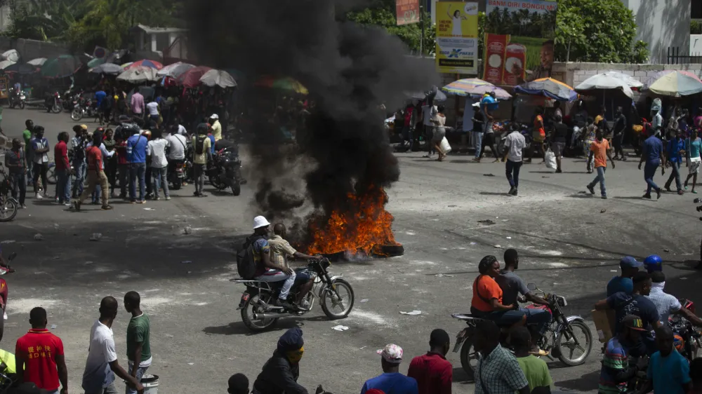 People walk around burning tires set up by taxi drivers to protest the country's fuel shortage in Port-au-Prince, Haiti, Wednesday, July 13, 2022. (AP Photo/Odelyn Joseph)