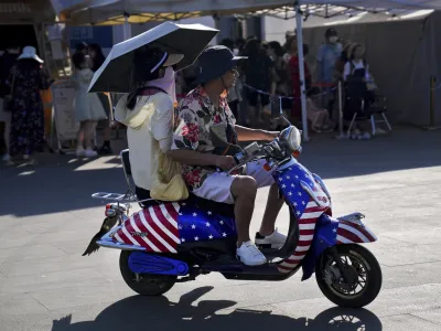 A Chinese couple ride on an electric bike with decals of the American flag, passing by visitors waiting in line to board a ferry at Erhai lake in Dali, in southwestern China's Yunnan province on Saturday, July 16, 2022. Treasury Secretary Janet Yellen said Tuesday the U.S. and South Korea should deepen their trade ties to avoid letting other countries use their market positions to unfair advantage &mdash; calling out China by name. (AP Photo/Andy Wong)