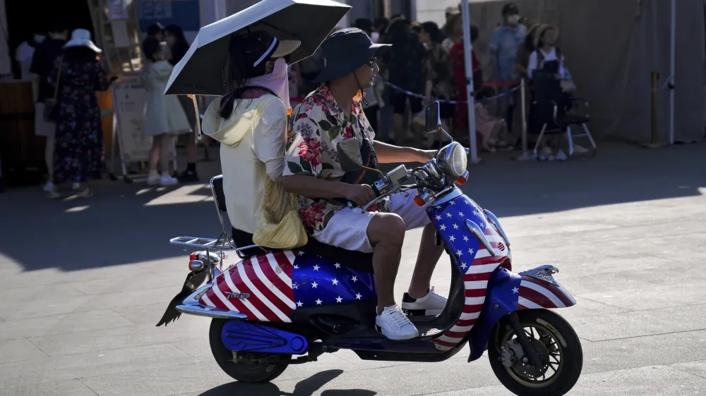 A Chinese couple ride on an electric bike with decals of the American flag, passing by visitors waiting in line to board a ferry at Erhai lake in Dali, in southwestern China's Yunnan province on Saturday, July 16, 2022. Treasury Secretary Janet Yellen said Tuesday the U.S. and South Korea should deepen their trade ties to avoid letting other countries use their market positions to unfair advantage &mdash; calling out China by name. (AP Photo/Andy Wong)