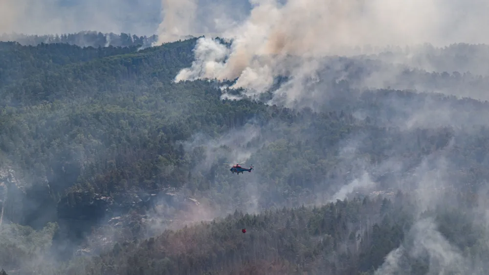 28 July 2022, Saxony, Schmilka: A cargo helicopter from Austria flies with an external water tank to extinguish a forest fire at the Saxon Switzerland National Park. Photo: Robert Michael/dpa