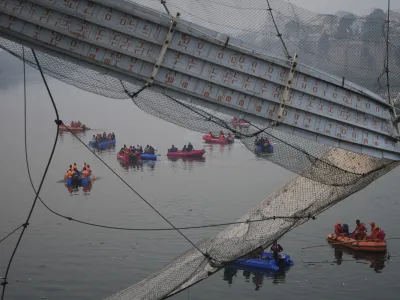 Rescuers on boats search in the Machchu river next to a cable suspension bridge that collapsed in Morbi town of western state Gujarat, India, Monday, Oct. 31, 2022. The century-old cable suspension bridge collapsed into the river Sunday evening, sending hundreds plunging in the water, officials said. (AP Photo/Ajit Solanki)