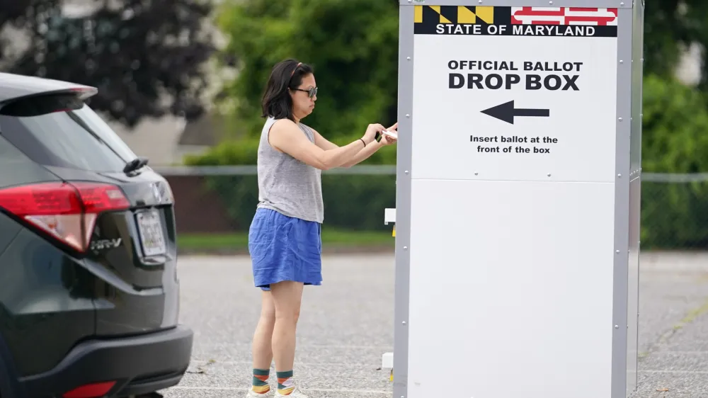 FILE - A woman drops a ballot into a drop box while casting her vote during Maryland's primary election, Tuesday, July 19, 2022, in Baltimore.  On Friday, Nov. 11, The Associated Press reported on stories circulating online incorrectly claiming a candidate winning an election with a majority of mailed ballots is proof of fraud. (AP Photo/Julio Cortez, File)