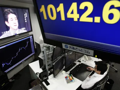 An employee of a foreign exchange trading company looks at monitors under an electronic board displaying the Nikkei share average as a television set shows Japan's incoming Prime Minister and the leader of Liberal Democratic Party (LDP) Shinzo Abe speaking in Tokyo December 26, 2012. The yen fell to a 20-month low against the dollar on Wednesday, buoying the benchmark Nikkei stock average, as Japan ushers in a new prime minister eager to pursue drastic stimulus steps to drive the country's economy out of deflation. REUTERS/Yuriko Nakao (JAPAN - Tags: POLITICS BUSINESS EMPLOYMENT)
