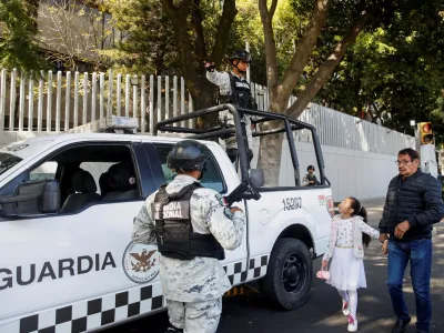 A man and a girl pass by as members of the National Guard keep watch following the detention of Mexican drug gang leader Ovidio Guzman, a son of incarcerated kingpin Joaquin "El Chapo" Guzman, who has been arrested by Mexican authorities, outside the building of the Attorney General's Office for Special Investigations on Organized Crime (FEMDO), in Mexico City, Mexico January 5, 2023. REUTERS/Raquel Cunha