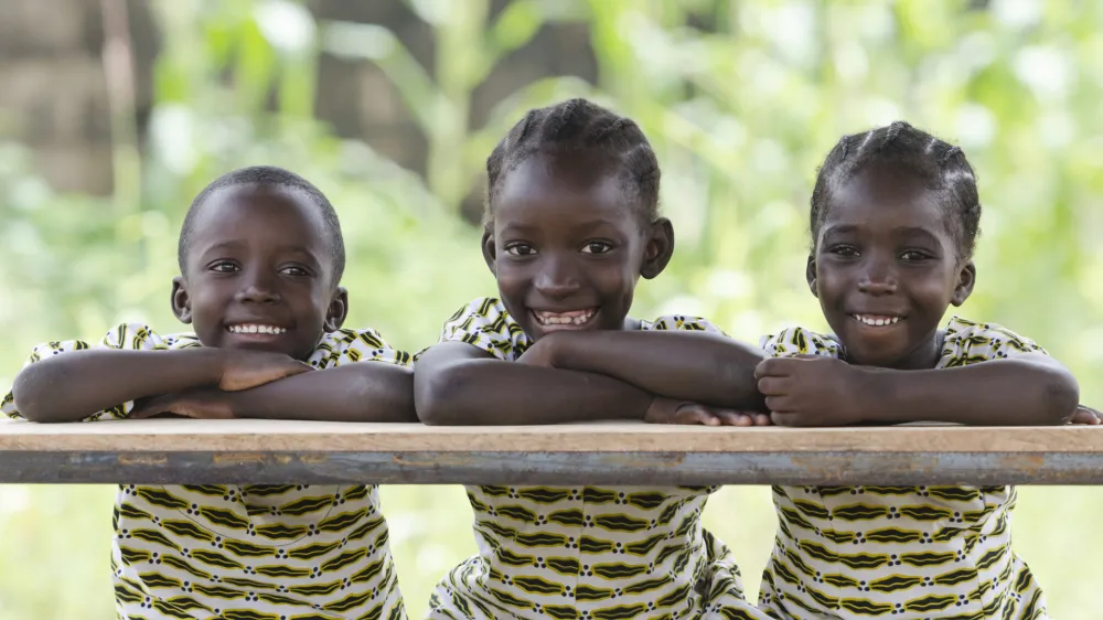 Three African children proudly sitting in their desk at school in Bamako, Mali. Candid outdoor shot of one boy and two girls learning their lessons at school.