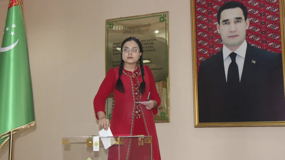 A woman wearing a national costume casts her ballot at a polling station with a portrait of President Serdar Berdymukhamedov, who was elected last year to succeed his father who had run the isolated ex-Soviet country for more than a decade in Ashgabat, Turkmenistan, Sunday, March 26, 2023. Voters in Turkmenistan have cast ballots for a new parliament that is expected to be opposition-free and loyal to the government of the gas-rich Central Asian nation. Sunday's election for 125 members included 258 candidates, put forward by three political parties or running independently. (AP Photo/Alexander Vershinin)