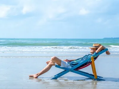 Asian man in casual clothing resting on beach chair at tropical beach. Happy guy sunbathing or nap on sunbed by the sea in sunny day. Young man relax and enjoy outdoor activity lifestyle on summer holiday vacation