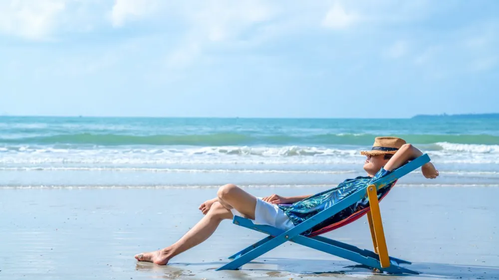 Asian man in casual clothing resting on beach chair at tropical beach. Happy guy sunbathing or nap on sunbed by the sea in sunny day. Young man relax and enjoy outdoor activity lifestyle on summer holiday vacation