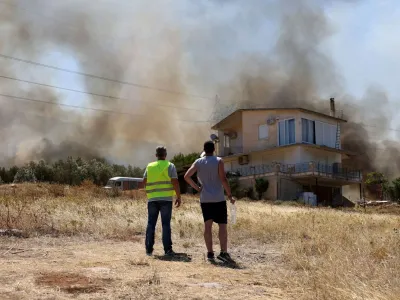 People stand in front of a house, as a wildfire burns in Kouvaras, Greece, July 17, 2023. REUTERS/Stelios Misinas   TPX IMAGES OF THE DAY