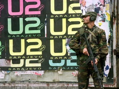 An Italian peacekeeper holds his rifle as he stands in front of wall covered with U2 posters in center Sarajevo September 21. The Irish band U2 will play at the Kosevo stadium on September 23 in Sarajevo's first major post-war rock concert. - PBEAHUMPBED
