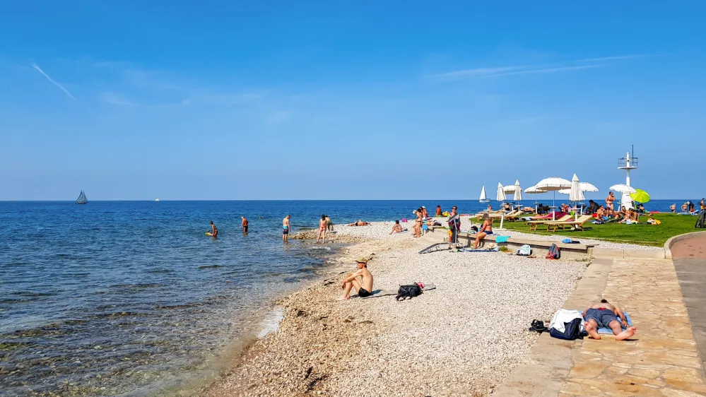 Izo, Slovenia &ndash; February 04, 2021: People on beach in Izola, Slovenia. Sunny summer day, palm trees, city, town, horizon, sea, vacation, travel.