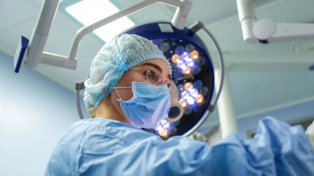 Female Doctor in Surgery Operating Hospital Room. Surgeon medic in protective work wear gloves, mask and cap.