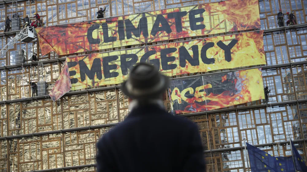 A man looks up as police and fire personnel move in to remove climate activists after they climbed the Europa building during a demonstration outside an EU summit meeting in Brussels, Thursday, Dec. 12, 2019. Greenpeace activists on Thursday scaled the European Union's new headquarters, unfurling a huge banner warning of a climate emergency hours before the bloc's leaders gather for a summit focused on plans to combat global warming.(AP Photo/Francisco Seco)