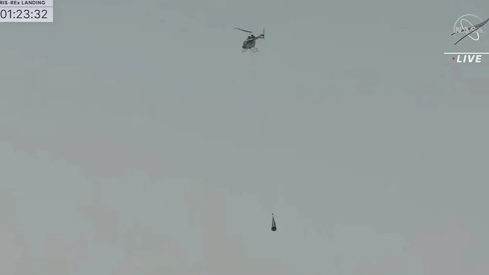 This image taken from video provided by NASA TV shows the capsule released by the Osiris-Rex spacecraft being lifted off by a helicopter after landing to Earth at Dugway Proving Ground, Utah, Sunday,Sept. 24 2023. (NASA TV via AP)