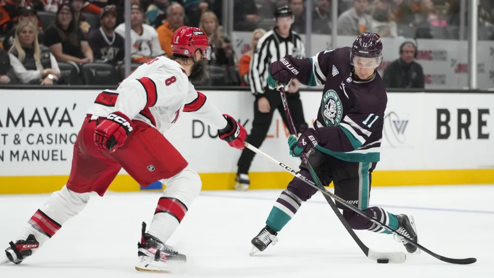 Anaheim Ducks' Trevor Zegras (11) shoots under defense by Carolina Hurricanes' Brent Burns (8) during the third period of an NHL hockey game Sunday, Oct. 15, 2023, in Anaheim, Calif. The Ducks won 6-3. (AP Photo/Jae C. Hong)