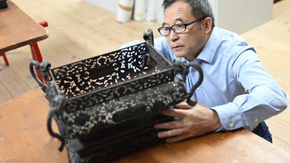 Kustos Guo Fuxiang si ogleduje enega od predmetov, ki jih je Sku&scaron;ek pred sto leti v Slovenijo pripeljal iz Kitajske.