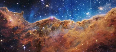 The "Cosmic Cliffs" of the Carina Nebula is seen in an image divided horizontally by an undulating line between a cloudscape forming a nebula along the bottom portion and a comparatively clear upper portion, with data from NASA's James Webb Space Telescope, a revolutionary apparatus designed to peer through the cosmos to the dawn of the universe and released July 12, 2022. Speckled across both portions is a starfield, showing innumerable stars of many sizes.  NASA, ESA, CSA, STScI, Webb ERO Production Team/Handout via REUTERS THIS IMAGE HAS BEEN SUPPLIED BY A THIRD PARTY.
