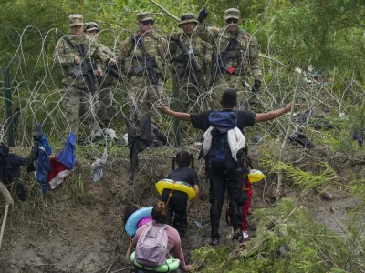 FILE - A migrant gestures to Texas National Guards standing behind razor wire on the bank of the Rio Grande river, seen from Matamoros, Mexico, May 11, 2023. (AP Photo/Fernando Llano, File)