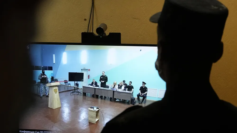 An officer stands in front of a TV screen showing Russian opposition leader Alexei Navalny, standing, speaking between his lawyers in a courtroom, via video link provided by the Russian Federal Penitentiary Service, during a preliminary hearing in the colony, in Melekhovo, Vladimir region, about 260 kilometers (163 miles) northeast of Moscow, Russia, on Monday, June 19, 2023. A Russian court has opened a new trial of imprisoned Russian opposition leader Alexei Navalny that could keep him behind bars for decades. (AP Photo/Alexander Zemlianichenko)
