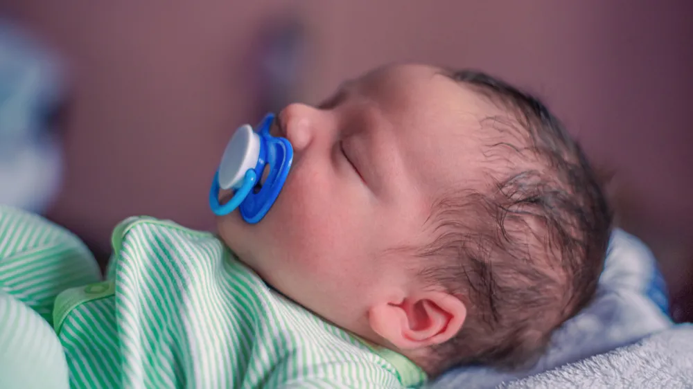 Face profile portrait of a sleeping newborn baby with a pacifier in his mouth