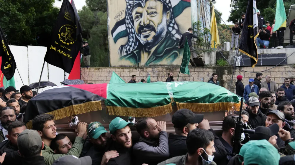 Mourners carry the coffin of Saleh Arouri, one of the top Hamas commanders, who was killed in an apparent Israeli strike Tuesday, as they pass in front of a graffiti that shows late Palestinian leader Yasser Arafat, during his funeral in Beirut, Lebanon, Thursday, Jan. 4, 2024. (AP Photo/Hussein Malla)
