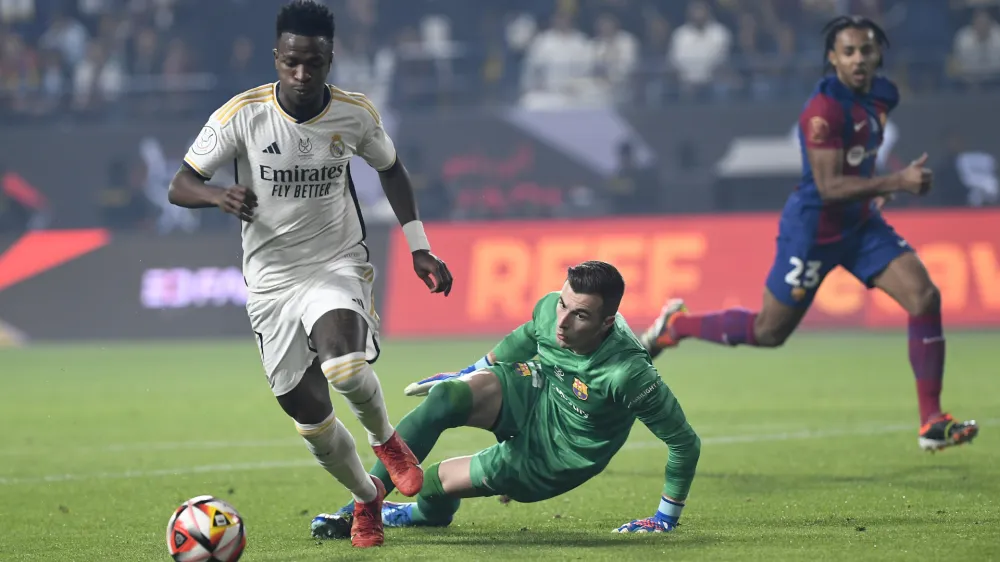 Real Madrid's Vinicius Junior, left, passes through Barcelona's goalkeeper Inaki Pena during the Spanish Super Cup final soccer match between Real Madrid and Barcelona at Al-Awwal Park Stadium in Riyadh, Saudi Arabia, Sunday, Jan. 14, 2024. (AP Photo)