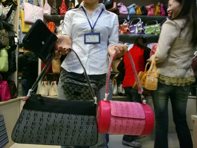 A sales clerk wearing a fanny pack with a Gucci label displays handbags bearing the Bulgari trademark name, as other bags showing the Yves Saint Laurent brand are seen behind, in Beijing's newly opened Silk Market commercial plaza Thursday March 31, 2005. Earlier this week inspectors confiscated more than 300 items in a raid on faked or pirated goods in the market. Responding to a new U.S. report that complains of "epidemic levels" of counterfeiting, China on Thursday insisted it is aggressively fighting the problem to protect both Chinese and foreign companies. (AP Photo/Elizabeth Dalziel)