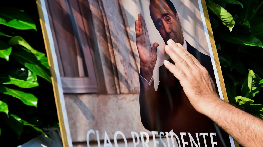A person touches a placard as people pay their respects outside former Italian Prime Minister Silvio Berlusconi's house, to which his body was transported following his death, in Arcore near Milan, Italy, June 12, 2023. REUTERS/Massimo Pinca