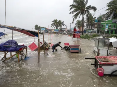 A man salvages a cart and other material as water flows on to the Kuakata beach on the coast of Bay of Bengal caused by the advancing Cyclone Remal in Barisal, Bangladesh, Sunday, May 26, 2024. (AP Photo/Abdul Goni)