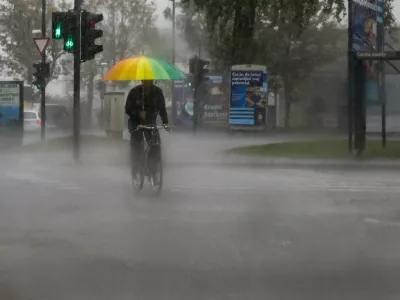kolesar in dežnik- 15.09.2022 - Močno deževje in poplave v Ljubljani - neurje - meteorna voda je zalila več garaž, podhodov, kletnih in stanovanjskih prostorov, skladi&scaron;č in poslovnih prostorov, pa tudi prostore osnovne &scaron;ole in vrtca, lekarne ter Narodno galerijo.Foto: Luka Cjuha