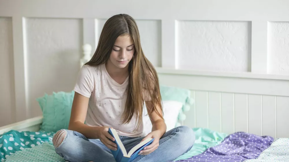 Adolescent teen girl reading a book while lying in bed at home in her bedroom. Lifestyle and learning photo of a cute teen / Foto: Yobro10