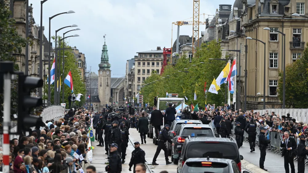 26 September 2024, Luxembourg: Spectators wait in the city center to see Pope Francis in the papamobile (Back) during his visit to Luxembourg. Photo: Harald Tittel/dpa