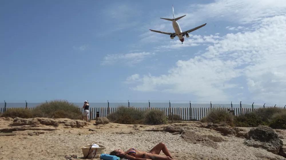 A woman sunbathes on the beach as an airplane lands at the Balearic Islands capital of Palma de Mallorca, Spain, Wednesday, July 29, 2020. Concerns over a new wave of coronavirus infections brought on by returning vacationers are wreaking havoc across Spain's tourism industry, particularly in the Balearic Islands following Britain's effective ban on travel to the country. (AP Photo/Joan Mateu