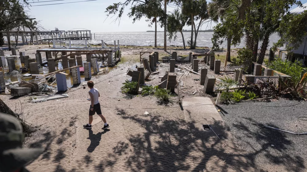 A person walks past building foundations along the water in the aftermath of Hurricane Helene, in Cedar Key, Fla., Friday, Sept. 27, 2024. (AP Photo/Gerald Herbert)