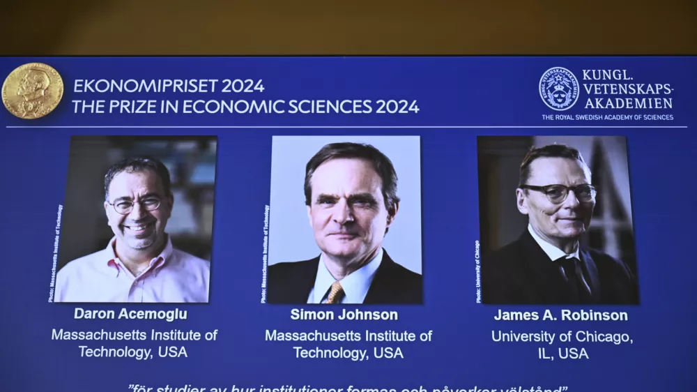 The Nobel memorial prize in economics awarded to Daron Acemoglu, Simon Johnson and James A Robinson, seen on screen, during a press meeting at the Royal Swedish Academy of Sciences in Stockholm, Sweden, Monday Oct. 14, 2024. (Christine Olsson/TT News Agency via AP)