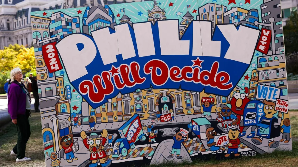 A woman stands next to a mural, part of the "To the Polls" temporary exhibition ahead of election day, at John F. Kennedy Plaza, known as Love Park, in Philadelphia, Pennsylvania, U.S., October 25, 2024. REUTERS/Hannah McKay