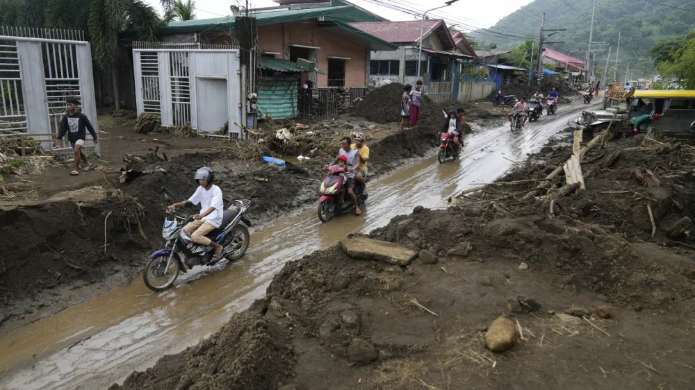 Residents ride motorcycles along a mud covered road after a landslide triggered by Tropical Storm Trami, recently struck Talisay, Batangas province, Philippines, Saturday, Oct. 26, 2024. (AP Photo/Aaron Favila)