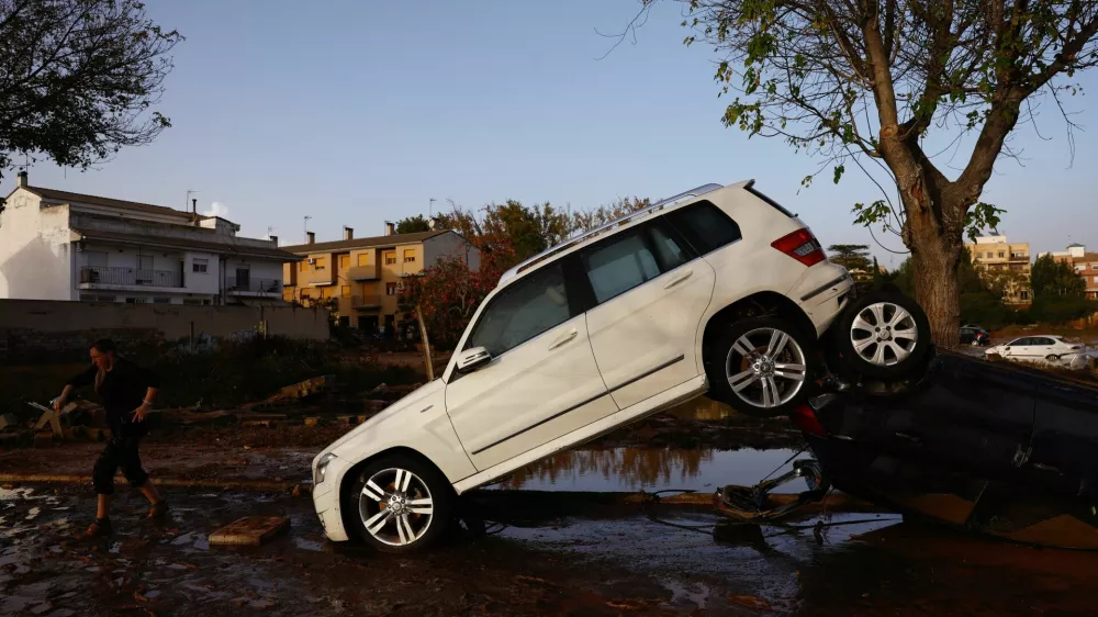 A person walks next to stacked cars after floods in Utiel, Spain, October 30, 2024. REUTERS/Susana Vera