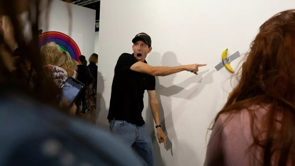 FILE PHOTO: A man poses for a photo next to a banana attached with duct-tape that replaces the artwork 'Comedian' by the artist Maurizio Cattelan, which was eaten by David Datuna, in Miami Beach, Florida, December 7, 2019. REUTERS/Eva Marie Uzcategui/File Photo