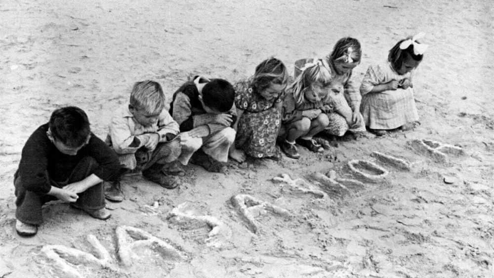 Okoli leta 1946 v Egiptu&nbsp;jugoslovanski otroci&nbsp;gledajo srbohrva&scaron;ke besede "na&scaron;a &scaron;kola" (na&scaron;a &scaron;ola), ki so jih zapisali v pesek,&nbsp;v begunskem tabori&scaron;ču&nbsp;Uprave združenih narodov za pomoč in obnovo (UNRRA) v Tolumbatu. UNRRA je delovala med leti 1943 in 1949, nato pa je bil njen mandat vključen v dolgoročno razvojno delo drugih agencij Združenih narodov. Delo UNRRA za otroke je prevzel Unicef. / Foto: arhiv Unicef / Foto: Arhiv Unicef