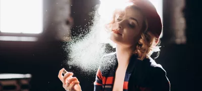 A beautiful blonde girl in a red beret holds a small bottle in her hands spraying perfume on herself enjoys armature. Backlight, soft focus.