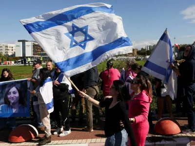 A woman waves an Israeli flag as people wait for the expected arrival of released Israeli hostages, who have been held in Gaza since the deadly October 7, 2023 attack by Hamas, as part of a prisoner-hostage exchange deal between Israel and Hamas, in Petah Tikva, Israel, January 25, 2025. REUTERS/Ronen Zvulun
