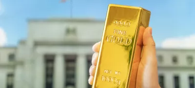 a gold bar in a man's hand against the background of the central bank, US Federal Reserve system. / Foto: Diy13