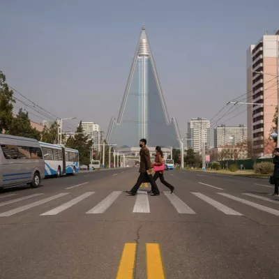 People wearing face masks walk across a street before the Ryugyong hotel (back C) on the occasion of the 108th birthday of late North Korean leader Kim Il Sung, known as the 'Day of the Sun', in Pyongyang on April 15, 2020.,Image: 513917283, License: Rights-managed, Restrictions:, Model Release: no
