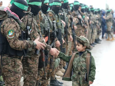 FILE PHOTO: A Palestinian Hamas militant shakes hands with a child as they stand guard as people gather on the day of the handover of hostages, including four held in Gaza since the deadly October 7 2023 attack, to members of the International Committee of the Red Cross (ICRC) as part of a ceasefire and a hostages-prisoners swap deal between Hamas and Israel, in Rafah in the southern Gaza Strip, February 22, 2025. REUTERS/Ramadan Abed/File Photo