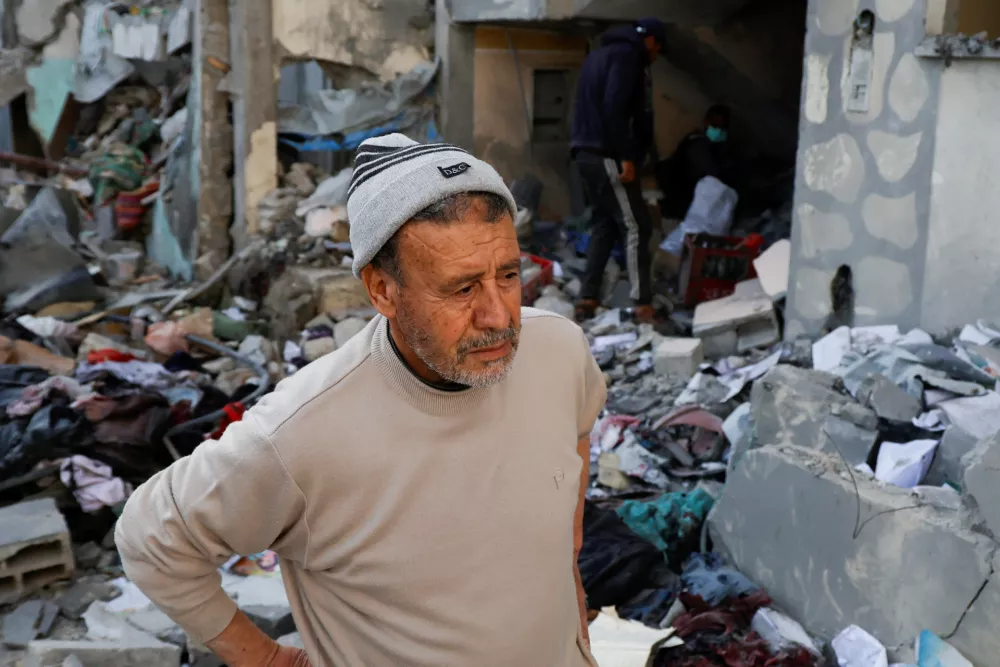 A man looks on as Palestinians inspect the site of an Israeli strike on a house, in Khan Younis in the southern Gaza Strip March 18, 2025. REUTERS/Hatem Khaled