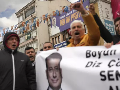 Backdropped by a billboard featuring a photo of Turkey's President Recep Tayyip Erdogan, people chant slogans as they protest outside the Vatan Security Department, where Istanbul Mayor Ekrem Imamoglu is expected to be taken following his arrest in Istanbul, Turkey, Wednesday, March 19, 2025. (AP Photo/Francisco Seco)